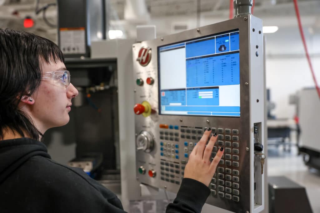 Taryn Reese operating a CNC machine wearing goggles.