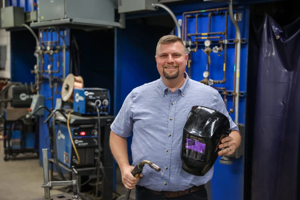 Paul Jensen holding welding equipment and smiling into the camera.