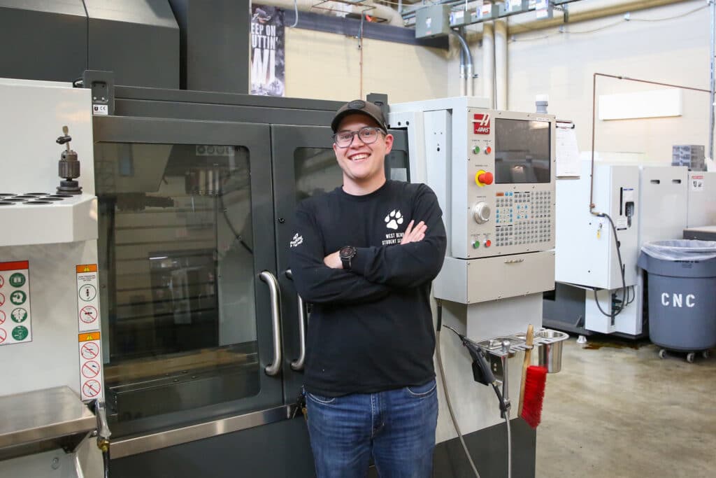 Charles (Chaz) Dreher III standing in front of a CNA machine.