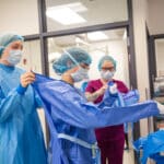 Surgical Technologist in the OP helping someone scrub in.